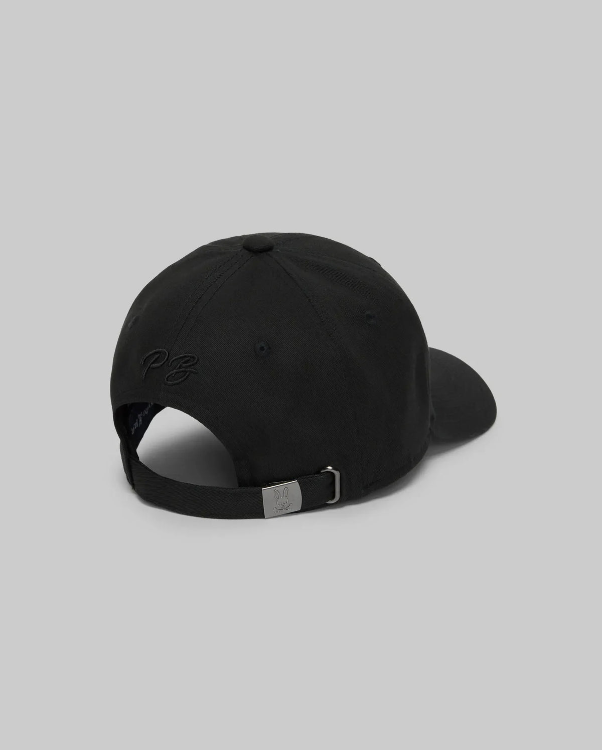 The Psycho Bunny MENS CYRUS BASEBALL CAP - MO1500045 is shown from the back on a gray background, featuring an adjustable metal strap and subtle embroidered text—an ideal way to add understated coastal charm to any outfit.