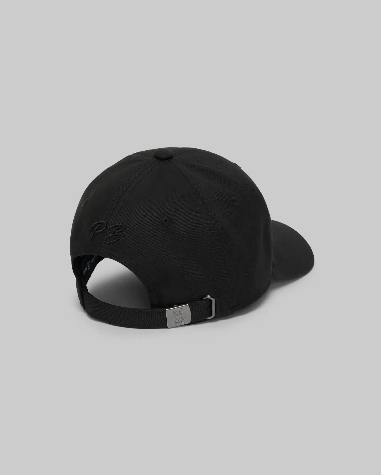 The Psycho Bunny MENS CYRUS BASEBALL CAP - MO1500045 is shown from the back on a gray background, featuring an adjustable metal strap and subtle embroidered text—an ideal way to add understated coastal charm to any outfit.