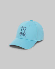 The Psycho Bunny MENS CYRUS BASEBALL CAP - MO1500045 is a light blue cap featuring a dark blue embroidered rabbit head above crossed bones on the front, shown against a plain gray background.