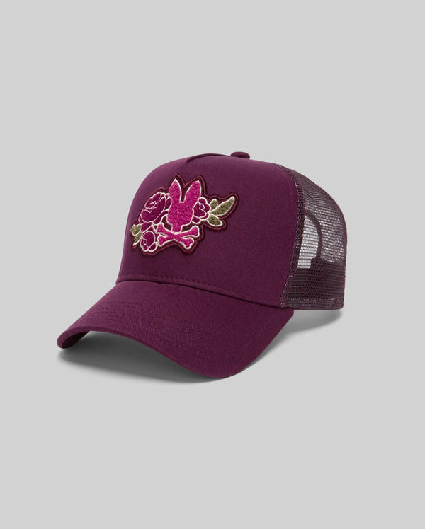 The Psycho Bunny MENS AUGUSTE TRUCKER CAP (MO1500050) features a maroon mesh back, a pink and green floral chenille patch on the front, and a snapback closure, displayed on a plain gray background.