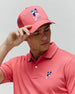Coral pink classic pique polo with striped collar/cuffs and a small embroidered multi-color Psycho Bunny skull logo on the left chest. A matching Mens Ara Trucker Cap features a large embroidered multi-color Psycho Bunny skull logo.