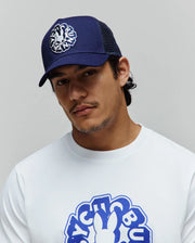 Mens Toby Trucker Cap in navy blue with white embroidered Psycho Bunny logo and mesh back, paired with a white classic fit jersey t-shirt featuring a large blue Psycho Bunny graphic on the chest.