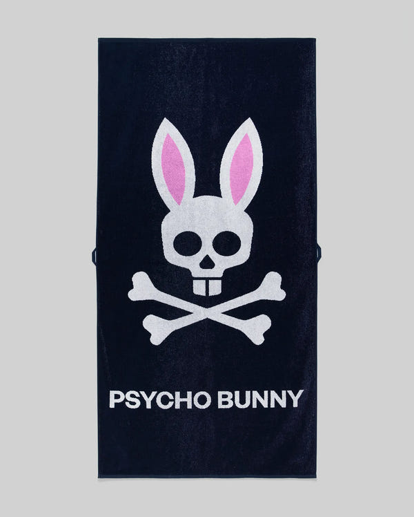 The Psycho Bunny MENS CLASSIC BUNNY TOWEL (MO1700004) is a dark towel with a white skull and crossbones topped by pink bunny ears above bold "PSYCHO BUNNY" lettering.