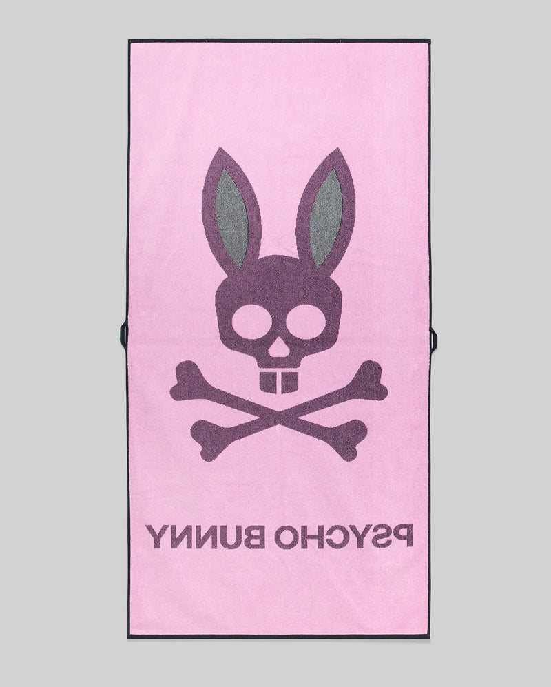 The Psycho Bunny MENS CLASSIC BUNNY TOWEL (MO1700004) is pink, showcasing a large dark gray bunny skull and crossbones with "PSYCHO BUNNY" below, all set against a plain gray background.