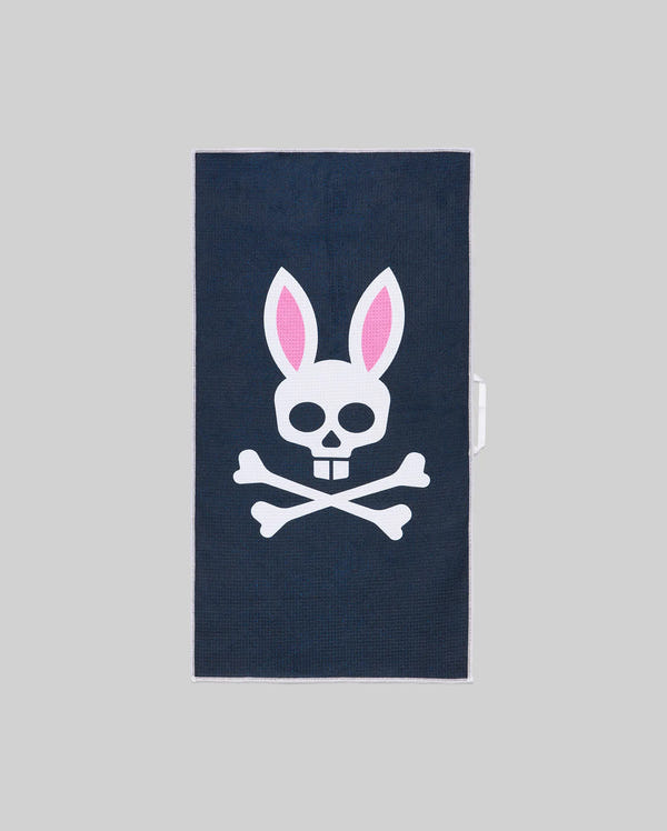The Psycho Bunny MENS MICROFIBER TOWEL - MO1700007 is dark blue, featuring a white skull with pink-eared bunny ears above crossed bones, set against a plain gray background.