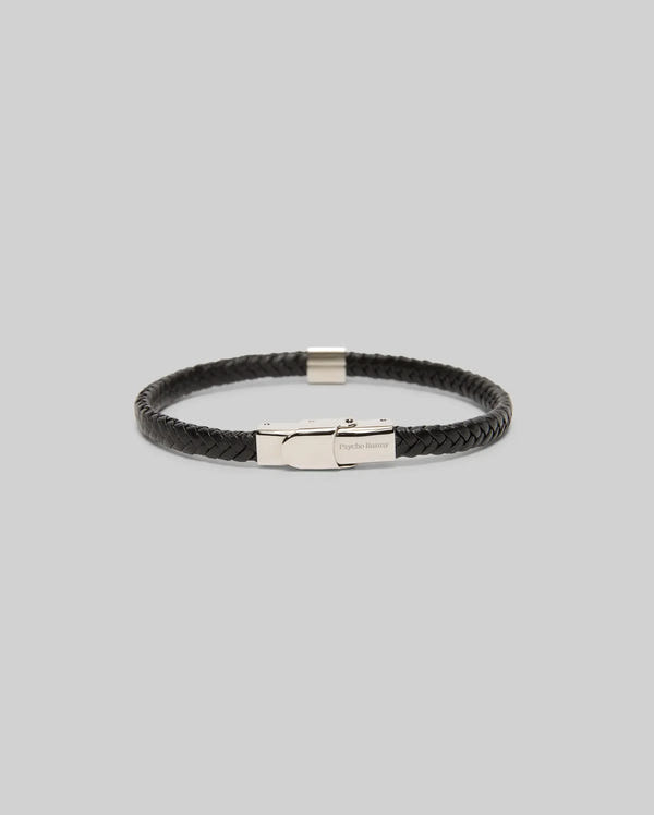 The Psycho Bunny MENS LEATHER BRAIDED BRACELET - MO1700020 features black braided leather, a hinged clasp, and bunny-engraved hardware, shown on a light grey background.