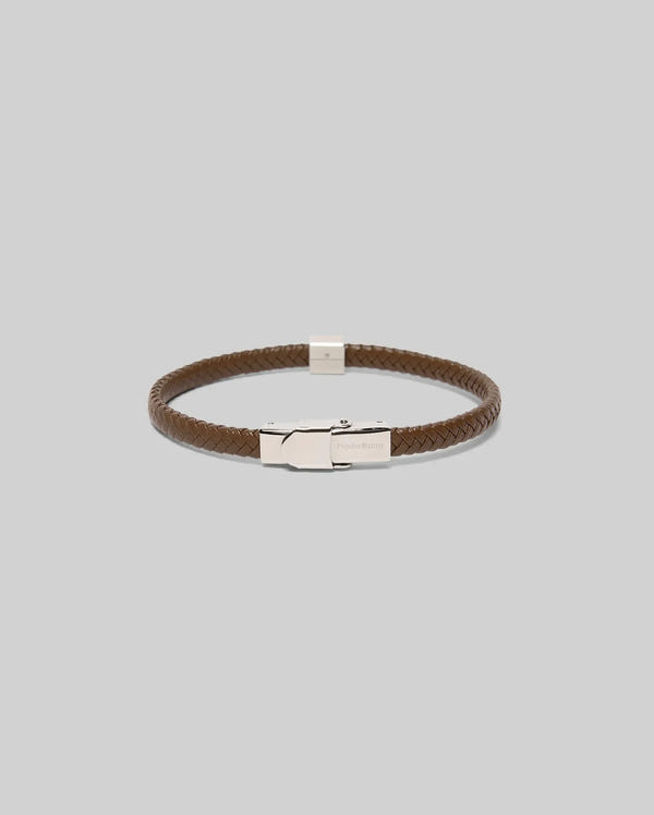 The Psycho Bunny MENS LEATHER BRAIDED BRACELET - MO1700020 features brown braided leather, a silver clasp, and bunny-engraved hardware, shown on a plain light gray background.