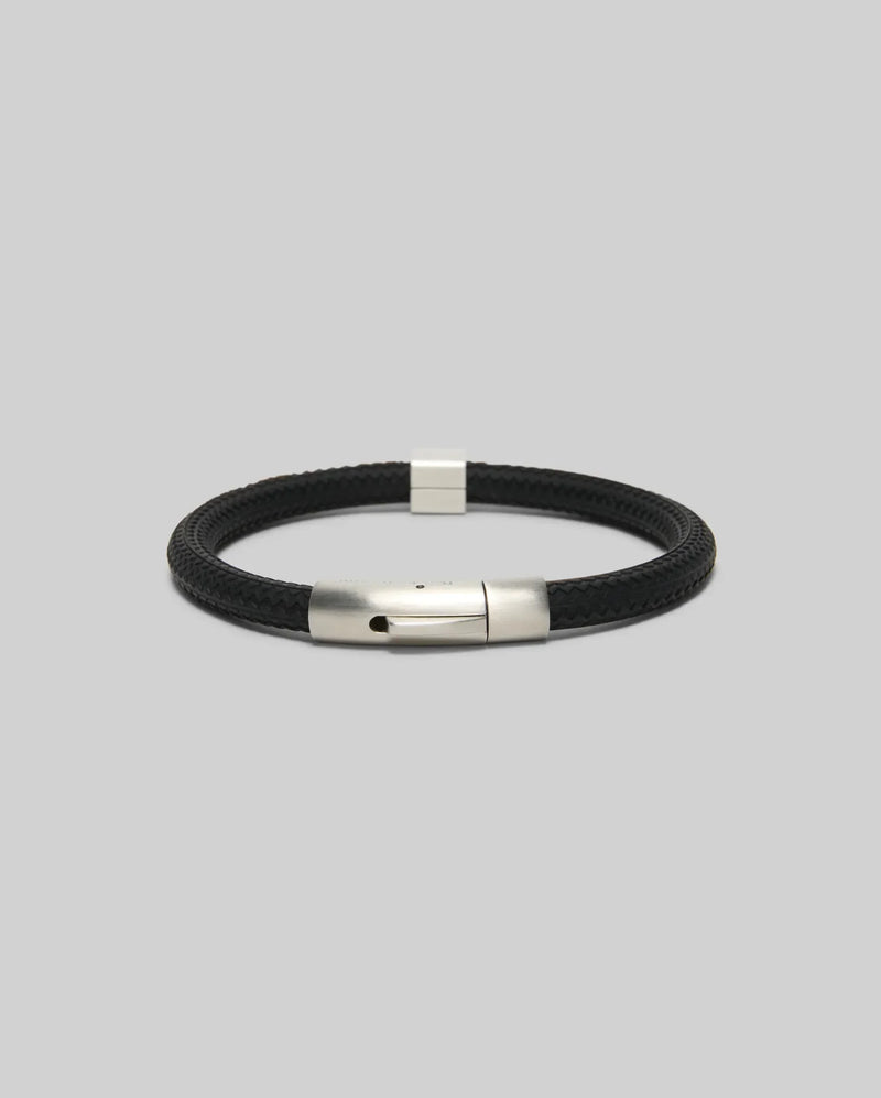 The Psycho Bunny MENS SILICONE BRACELET - MO1700025 features a black braided design with a sleek silver clasp, showcased on a plain light gray background.