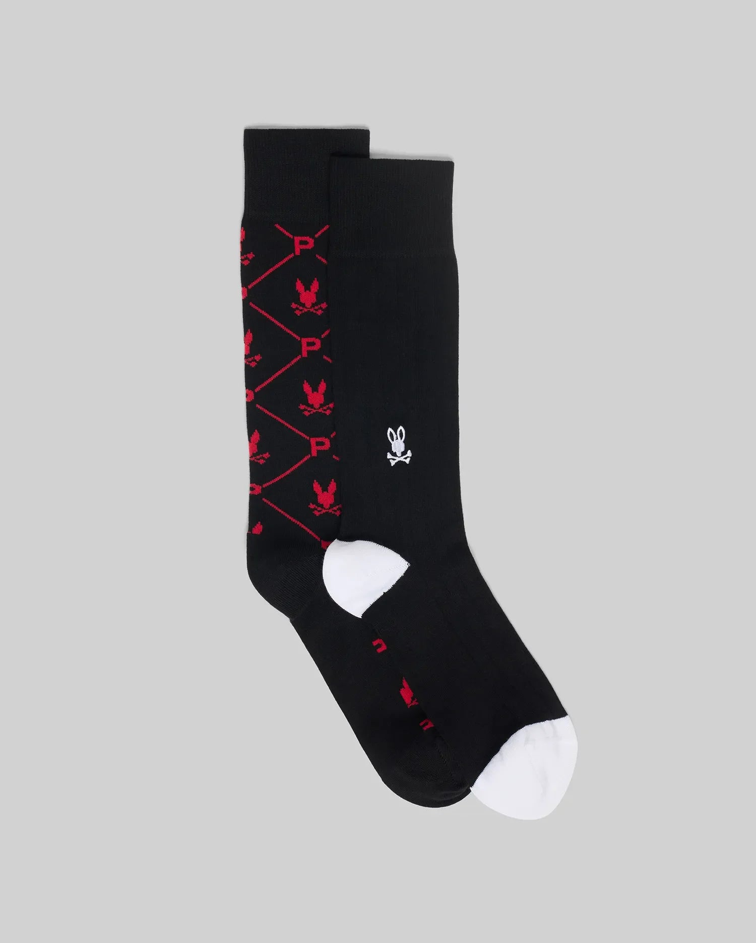 The Psycho Bunny MENS 2 PACK DRESS SOCK (MO2200005) features black socks: one with a white rabbit skull logo, the other with a diamond pattern, red rabbit skulls, and 