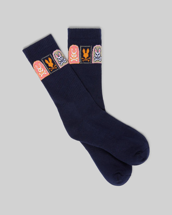 The Psycho Bunny MENS SUNDEW GRAPHIC SPORT SOCK (MO2200020) features navy blue Pima cotton, light gray background, and four colorful bunny graphics on the cuffs—each in a distinct color square—for playful comfort.