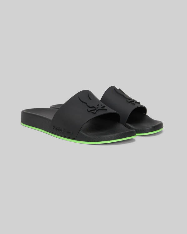 The Psycho Bunny MENS CONTRAST SOLE SLIDES (MO2400007) are black slide sandals with a raised logo on the strap, a green stripe on the sole, and a molded footbed for comfort, shown against a plain gray background.