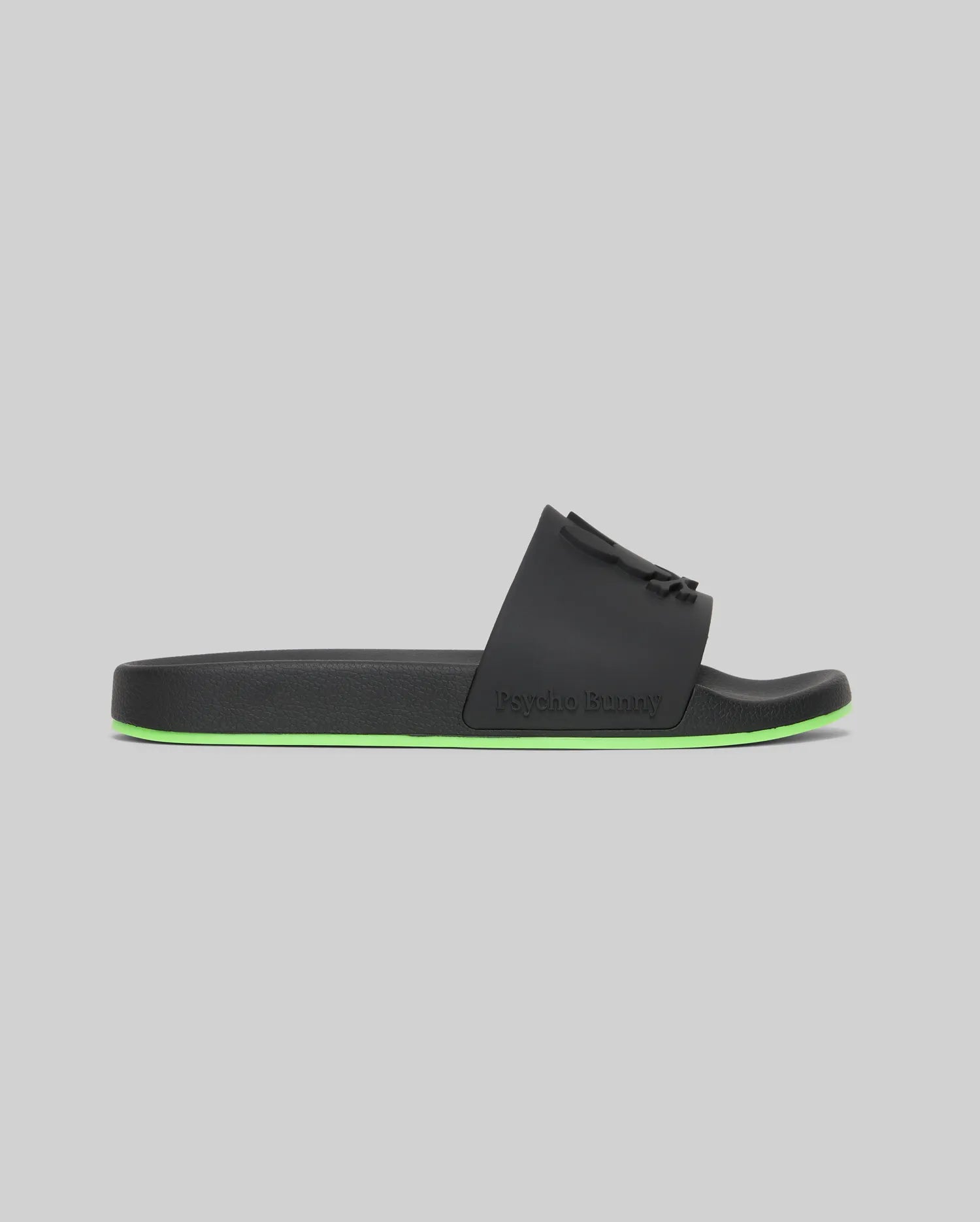 The Psycho Bunny MENS CONTRAST SOLE SLIDES - MO2400007 are black slide sandals with a wide strap, embossed logo, neon green sole, and molded footbed for comfort—ideal for laidback style and shown on a light gray background.
