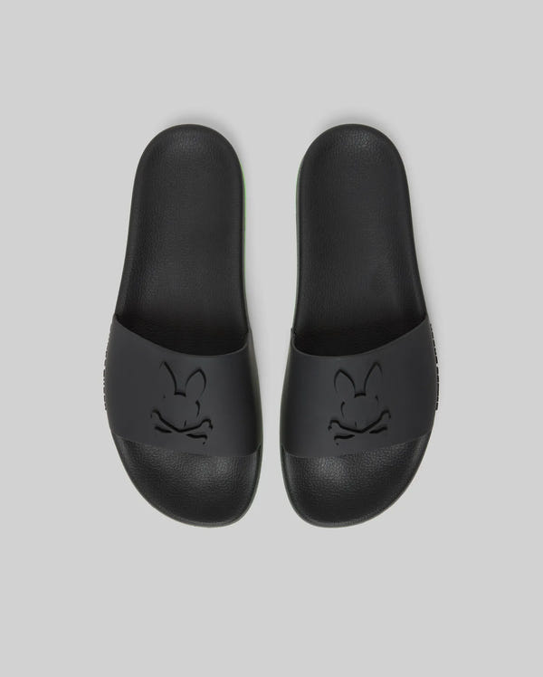 Psycho Bunny MENS CONTRAST SOLE SLIDES - MO2400007: Black slides with an embossed cartoon bunny face on the wide strap, molded footbed for support, shown on a plain light gray background.