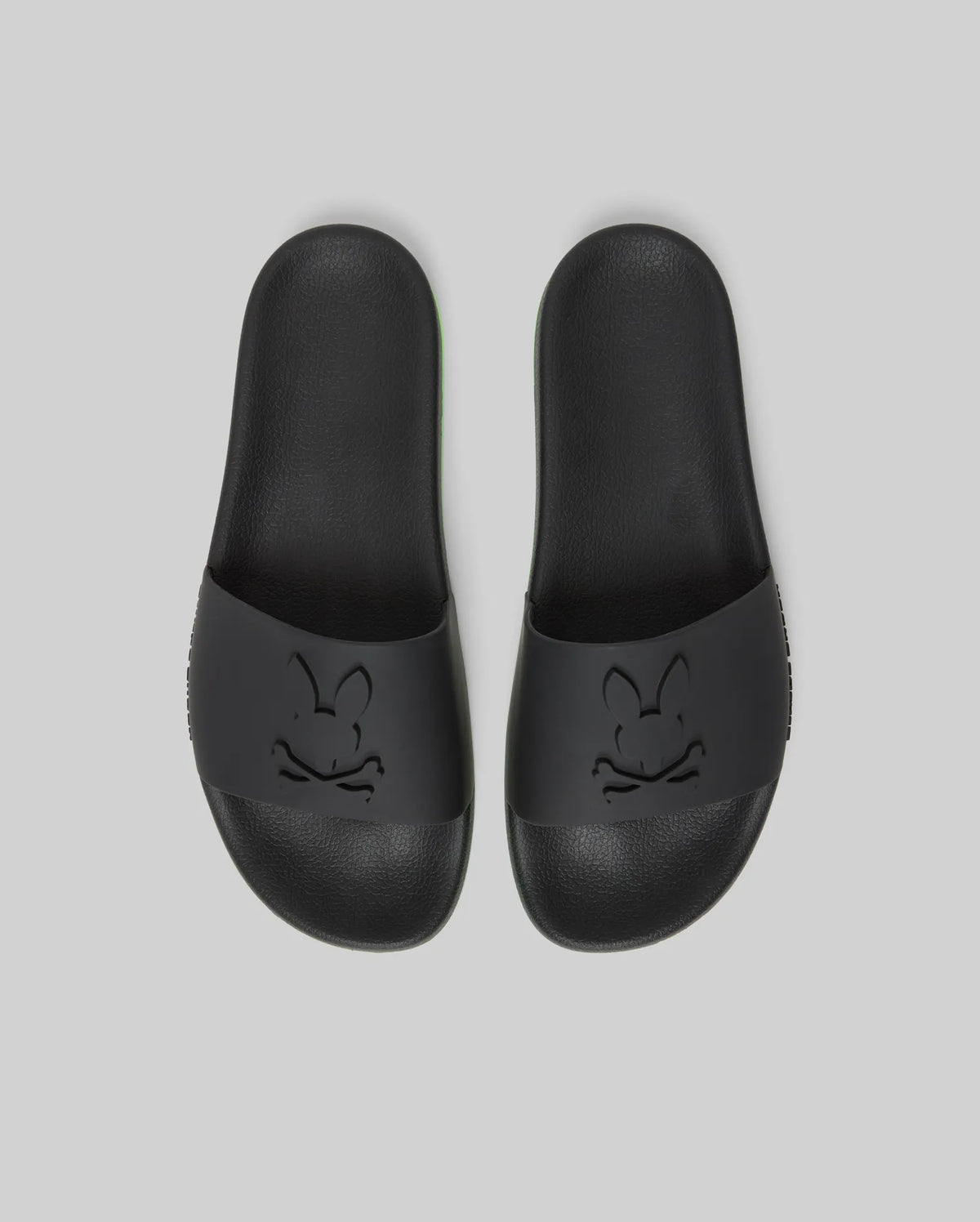 Psycho Bunny MENS CONTRAST SOLE SLIDES - MO2400007: Black slides with an embossed cartoon bunny face on the wide strap, molded footbed for support, shown on a plain light gray background.