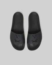 Psycho Bunny MENS CONTRAST SOLE SLIDES - MO2400007: Black slides with an embossed cartoon bunny face on the wide strap, molded footbed for support, shown on a plain light gray background.