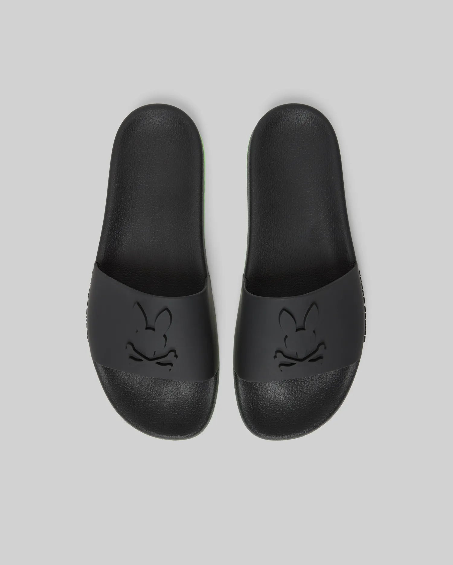 Psycho Bunny MENS CONTRAST SOLE SLIDES - MO2400007: Black slides with an embossed cartoon bunny face on the wide strap, molded footbed for support, shown on a plain light gray background.