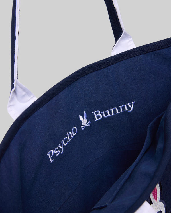 Close-up of the Psycho Bunny MENS CANVAS TOTE BAG - MO2400016 in dark blue with white handles. Features "Psycho Bunny" and a bunny skull logo embroidered inside—an ideal match for premium athleisure looks.