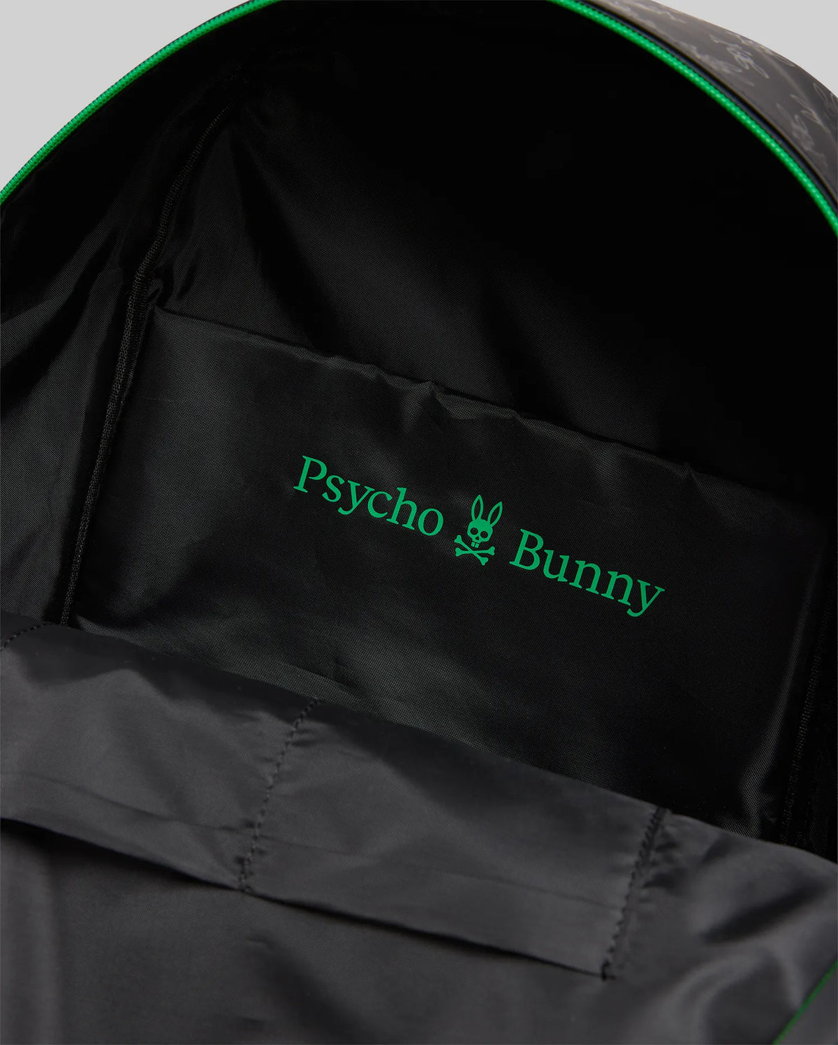 Bunny Backpack in black with a subtle tonal exterior pattern, vibrant green zipper trim, and a smooth black interior lining featuring a prominent green Psycho Bunny skull logo and text.