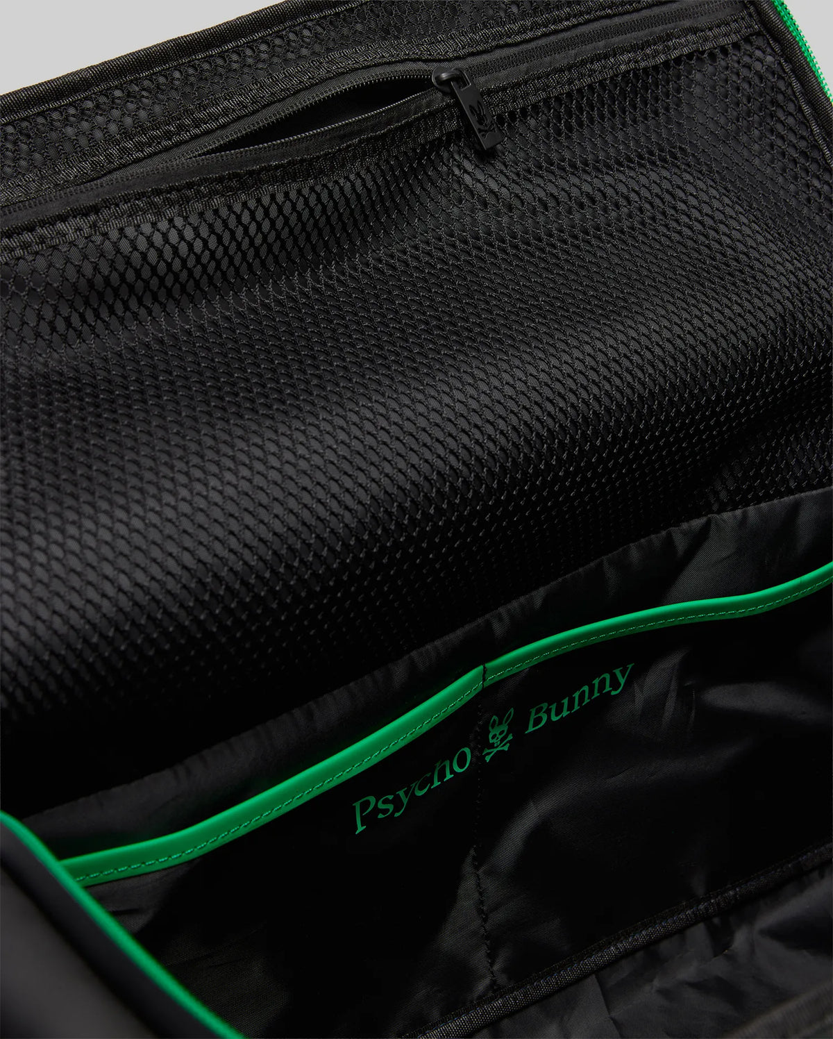 Black Gym Bag MO2400095 interior featuring a large mesh pocket, zippered compartment, and vibrant green piping accenting the embroidered Psycho Bunny skull logo.