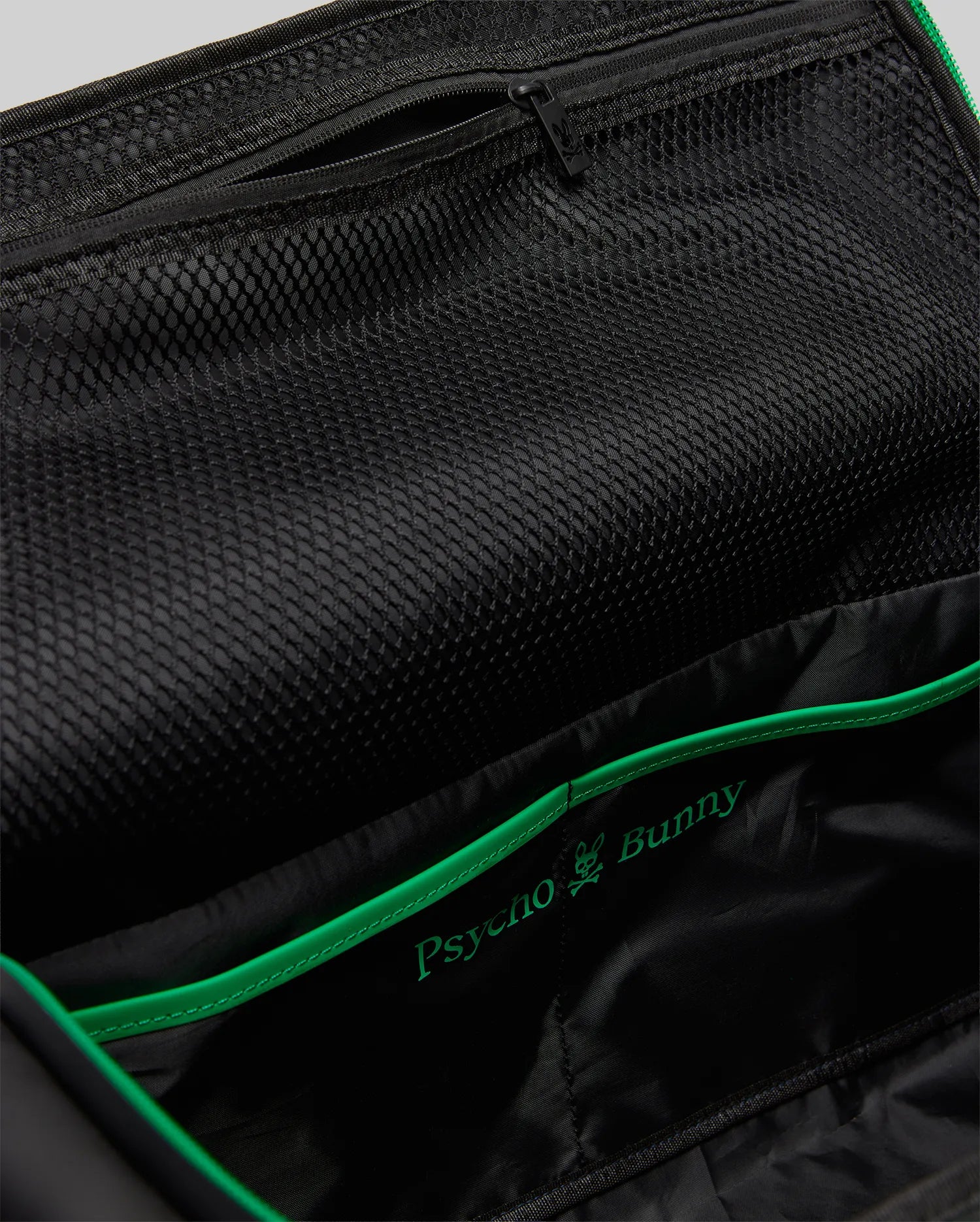 Black Gym Bag MO2400095 interior featuring a large mesh pocket, zippered compartment, and vibrant green piping accenting the embroidered Psycho Bunny skull logo.