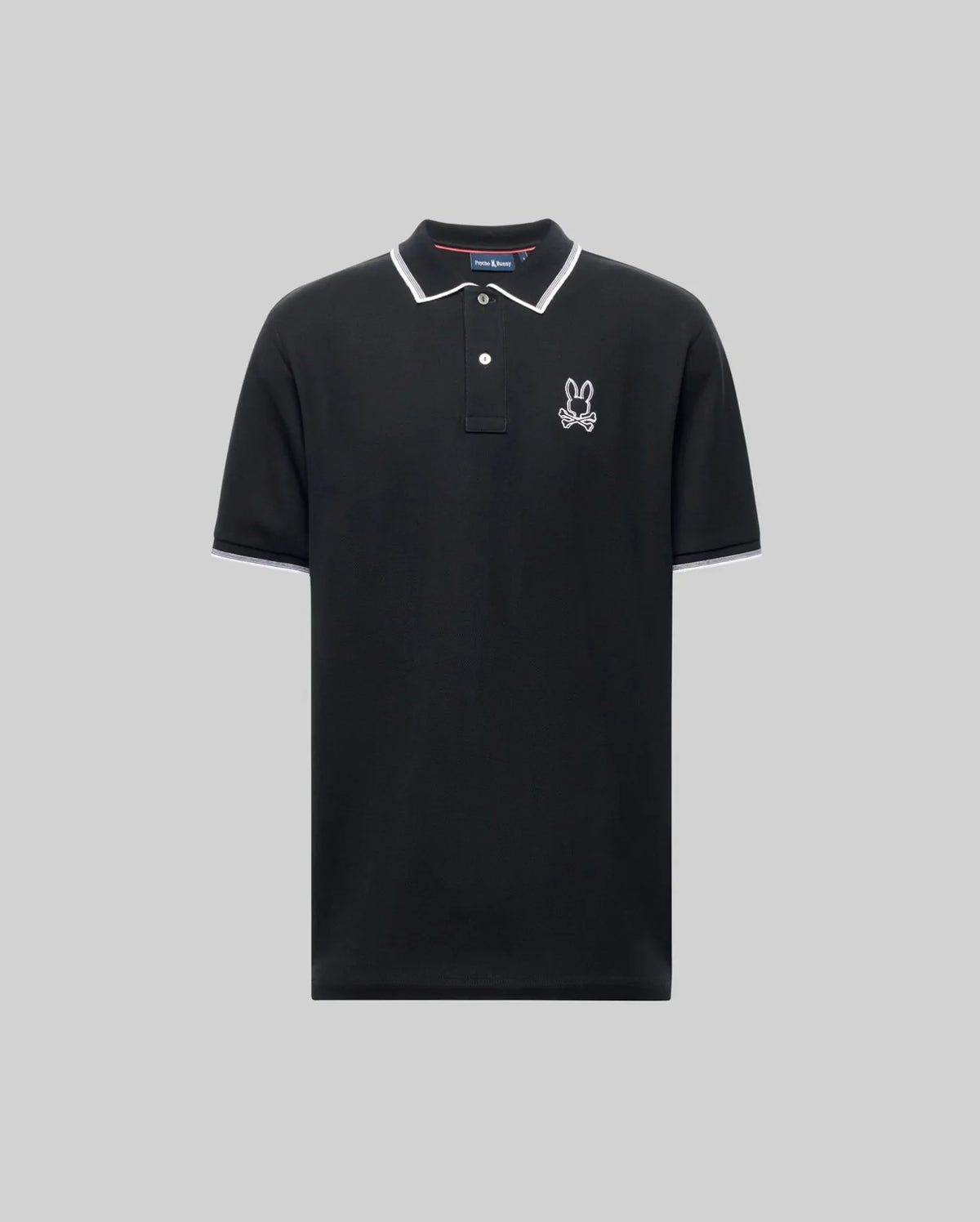 The Psycho Bunny MENS JUDE PIQUE POLO (MT0100012) is a black short-sleeve shirt with white trim on the collar and sleeves, an embroidered bunny logo on the left chest, and is made from soft Pima cotton for comfort. Displayed on a light gray background.