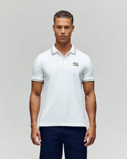 A man faces forward in dark pants and a Psycho Bunny MENS ARCHIVE NEON BUNNY POLO MT0100018—a regular fit white, 100% Pima cotton short-sleeve shirt featuring a small embroidered Bunny on the chest—against a plain light background.