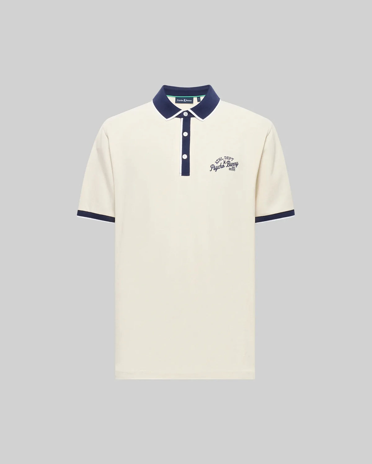 The Psycho Bunny MENS MATTEO PIQUE POLO (MT0100024) is a cream Pima cotton short-sleeve shirt with a navy collar, cuffs, and button placket featuring Mother-of-Pearl buttons. Navy cursive text accents the left chest; shown on a gray background.