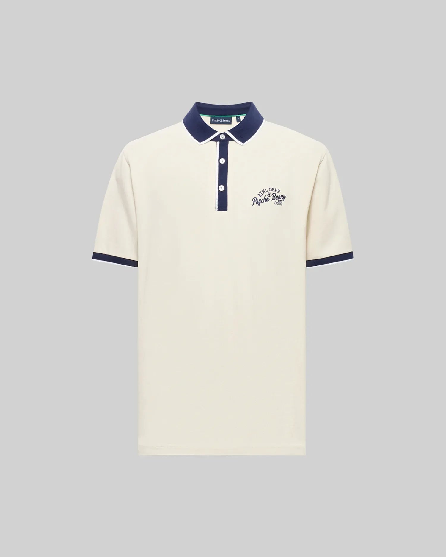 The Psycho Bunny MENS MATTEO PIQUE POLO (MT0100024) is a cream Pima cotton short-sleeve shirt with a navy collar, cuffs, and button placket featuring Mother-of-Pearl buttons. Navy cursive text accents the left chest; shown on a gray background.