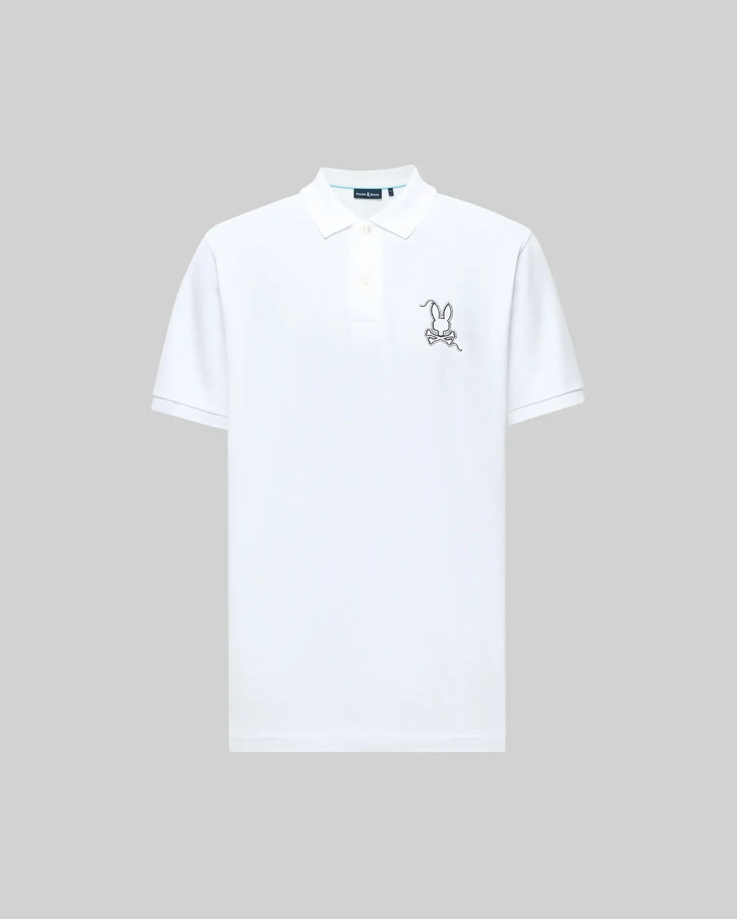 The Psycho Bunny MENS CYRUS PIQUE POLO (MT0100056) is a plain white Pima cotton shirt with a collar and buttons, featuring a small, outlined cartoon bunny with glasses embroidered on the left chest. Light gray background.