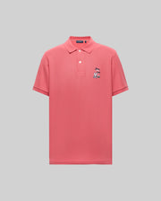The Psycho Bunny MENS SONNY PIQUE POLO - MT0100094 is a plain pink short-sleeve Pima cotton shirt with a collar, three buttons, and a charming cartoon character chest embroidery. The background is light gray.