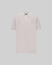 The Psycho Bunny MENS CASSIAN PIQUE POLO (MT0100098) is a light beige, short-sleeve Pima cotton shirt with a collar, two buttons, and a blue and white embroidered bunny logo on the left chest, shown on a plain gray background.