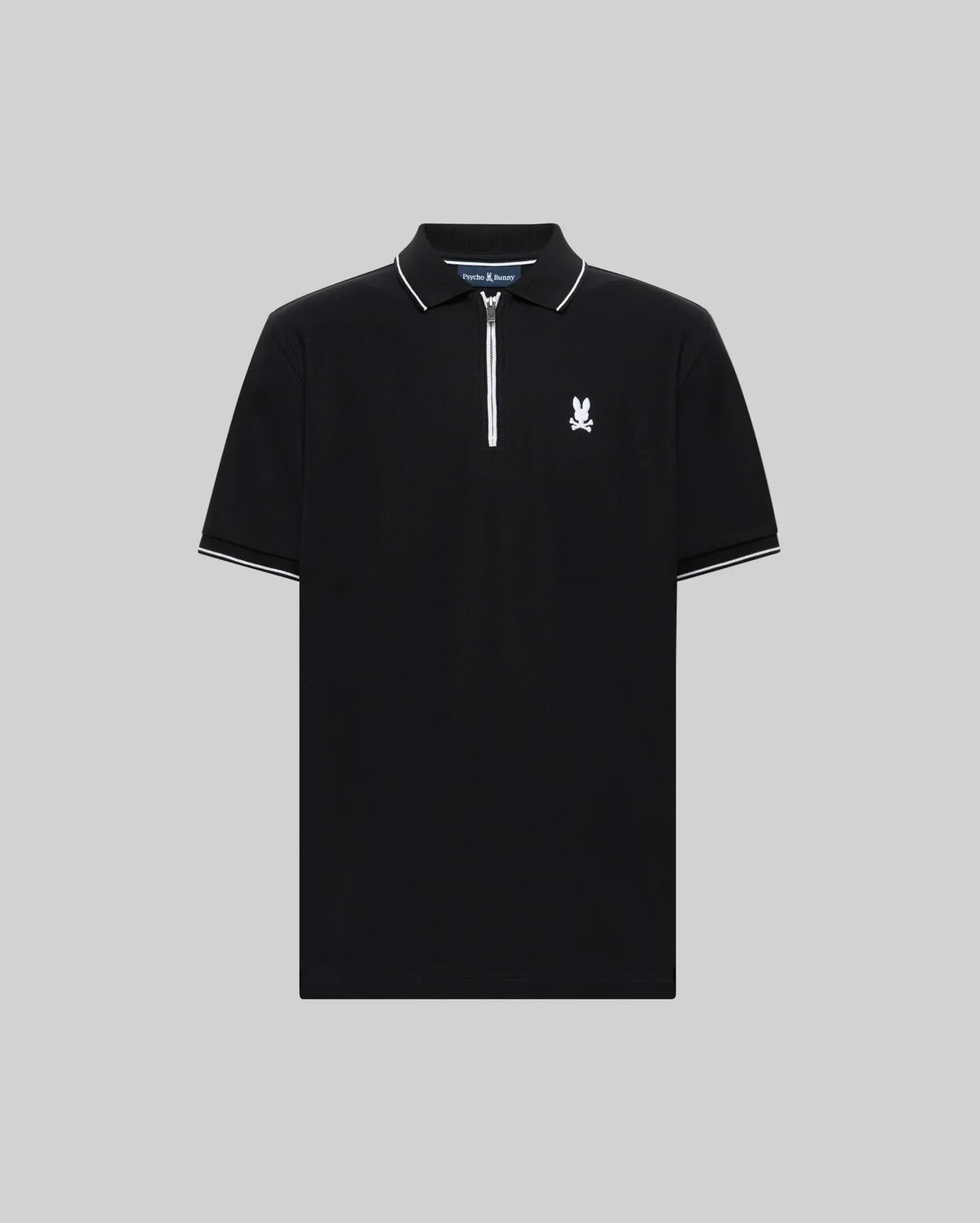 The Psycho Bunny MENS DANE ZIP PIQUE POLO (MT0100103) features black short sleeves, a white zip placket collar, white sleeve trim, and a small white graphic logo on the left chest, shown against a plain gray background.