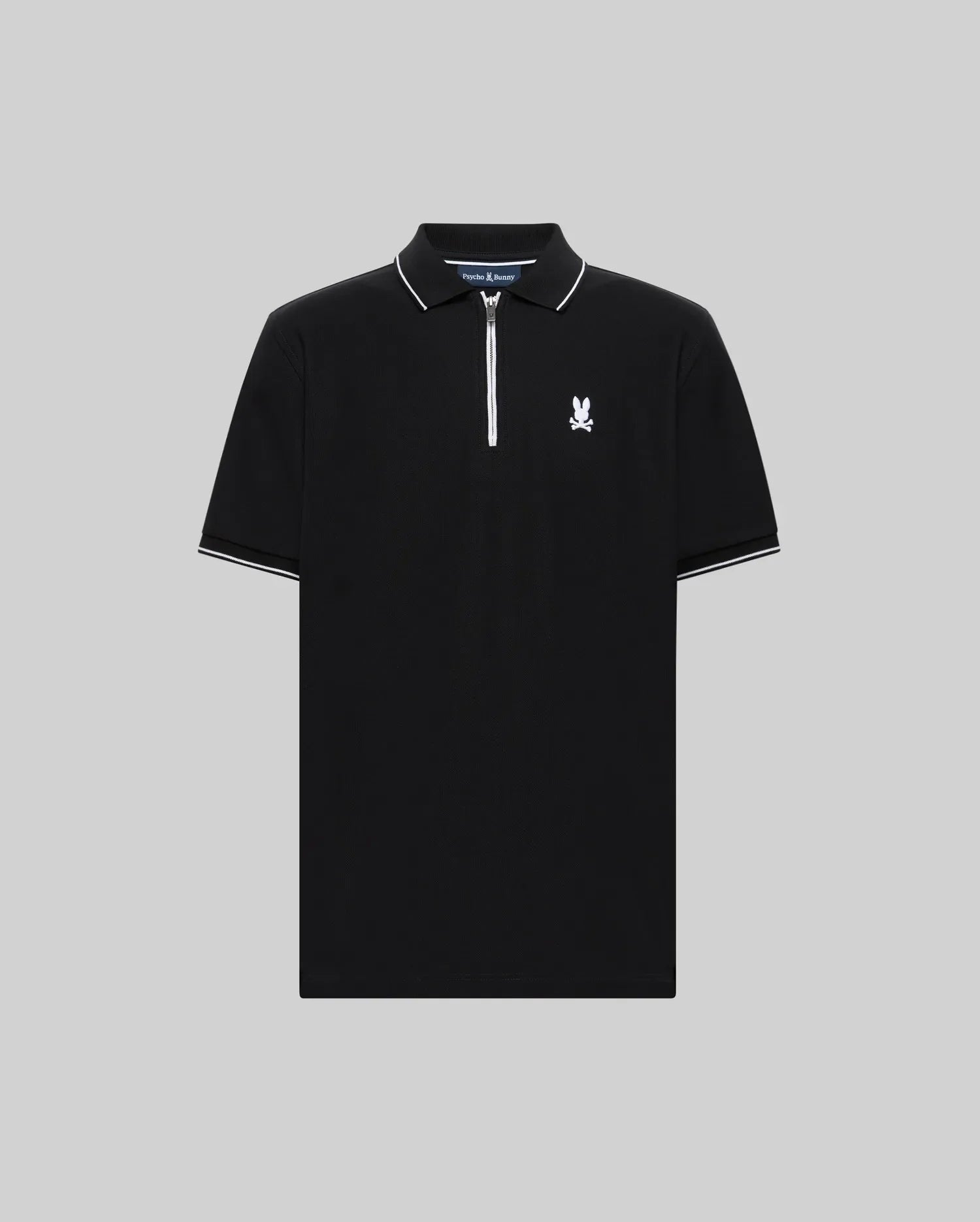 The Psycho Bunny MENS DANE ZIP PIQUE POLO (MT0100103) features black short sleeves, a white zip placket collar, white sleeve trim, and a small white graphic logo on the left chest, shown against a plain gray background.