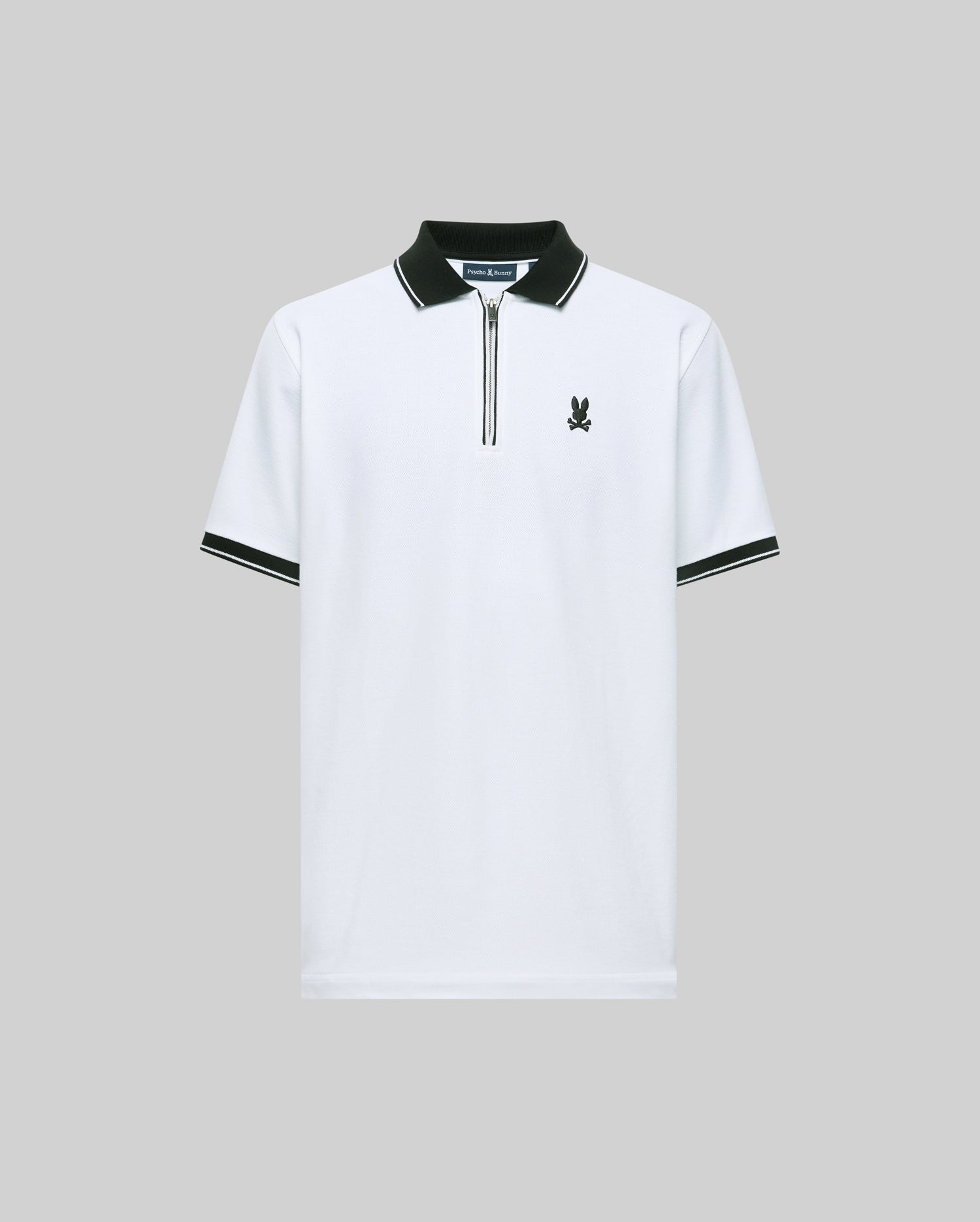 The Psycho Bunny MENS DANE ZIP PIQUE POLO (MT0100103) is a white regular-fit Pima cotton polo with a black collar, zipper, and sleeve trim. Features an embroidered bunny logo on the left chest, shown against a plain gray background.