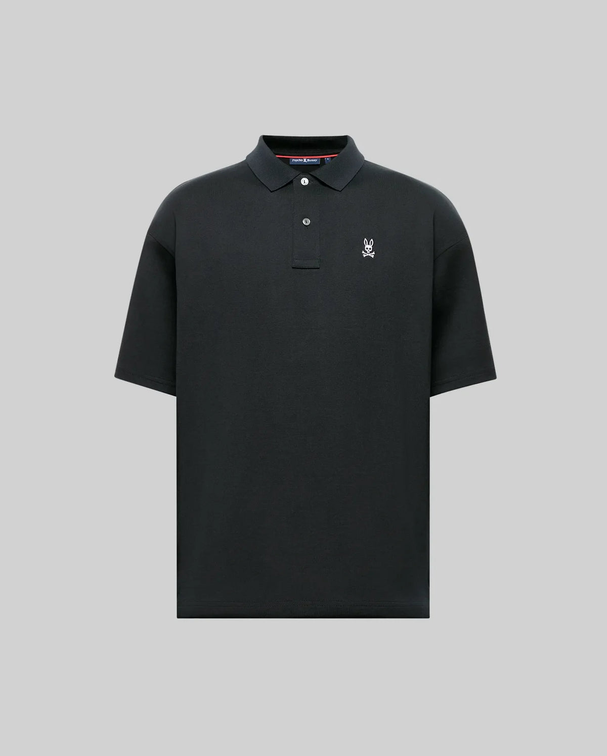 The MENS HENRY OVERSIZED FIT POLO - MT0100104 by Psycho Bunny is a black, short-sleeve Pima cotton polo with a collar, two buttons, and a small white embroidered bunny with crossed bones on the left chest. Displayed on a gray background.