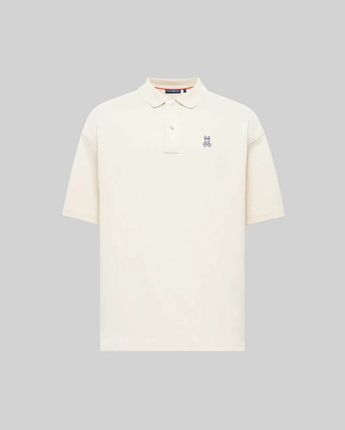 The Psycho Bunny MENS HENRY OVERSIZED FIT POLO (MT0100104) is a soft Pima cotton jersey shirt in plain off-white, with short sleeves, a collar, button placket, and small embroidered bunny logo on the chest. Displayed on a light gray background.
