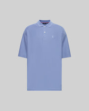 The Psycho Bunny MENS BENNY OVERSIZED FIT PIQUE POLO (MT0100105) is a light blue Pima cotton shirt with a collar, two-button neck, relaxed fit, and small white embroidered logo on the left chest. Displayed on a plain light grey background.
