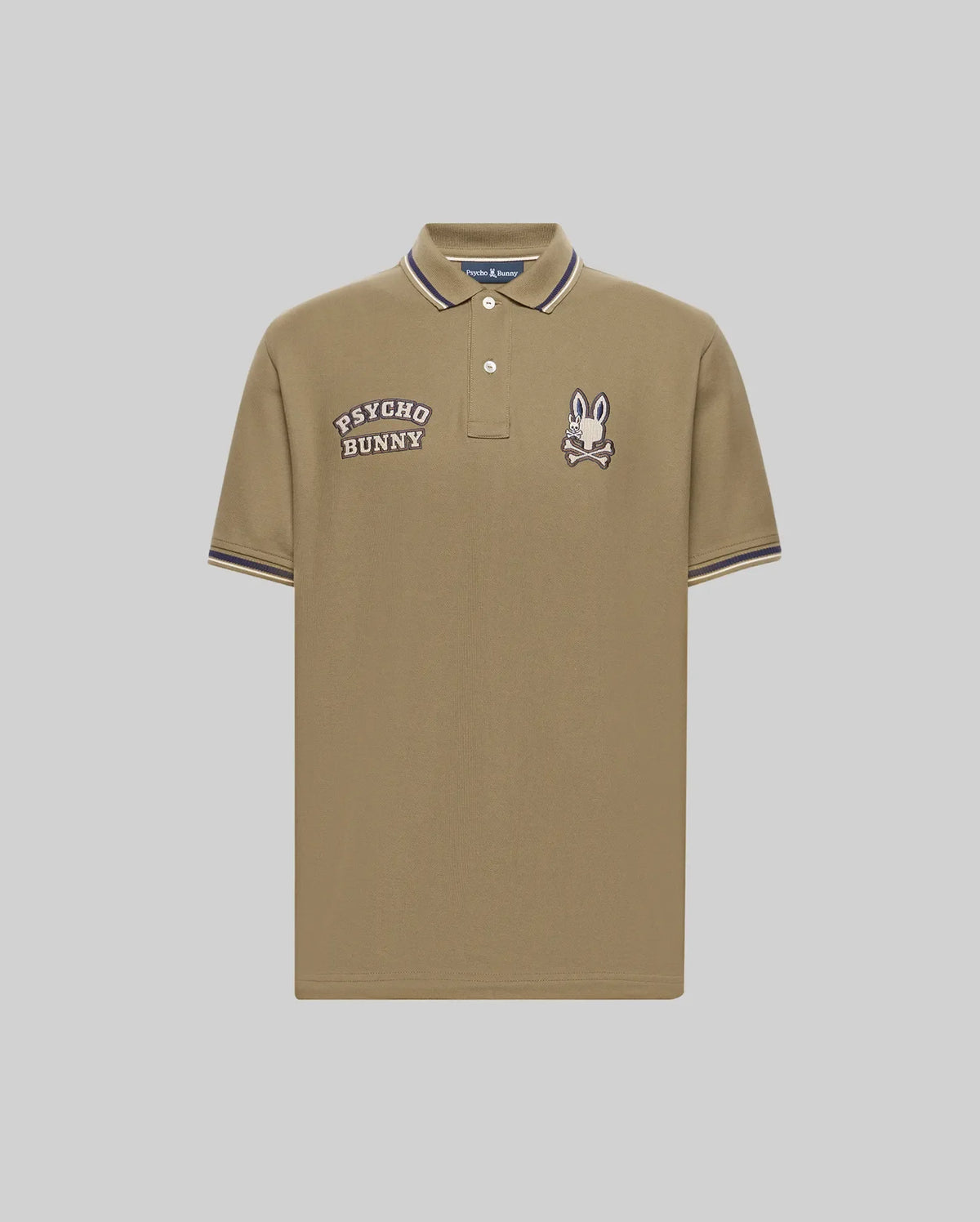 The Psycho Bunny Men's Wade Patch Pique Polo Shirt (MT0100109) is made from khaki Pima cotton with white buttons, "PSYCHO BUNNY" text, an embroidered Bunny skull logo patch on the chest, and white/navy striped collar and sleeve trim.
