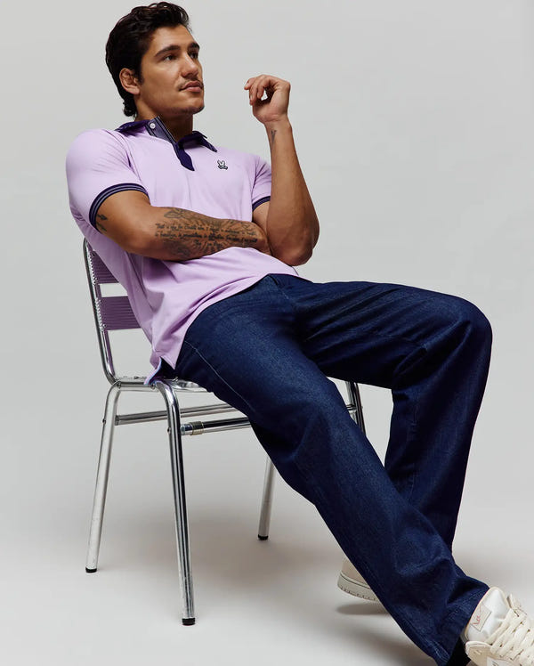 Mens Kenyon Pique Polo, a classic fit lavender pique polo with a navy blue collar and striped cuffs, featuring a small embroidered Psycho Bunny skull logo on the left chest.
