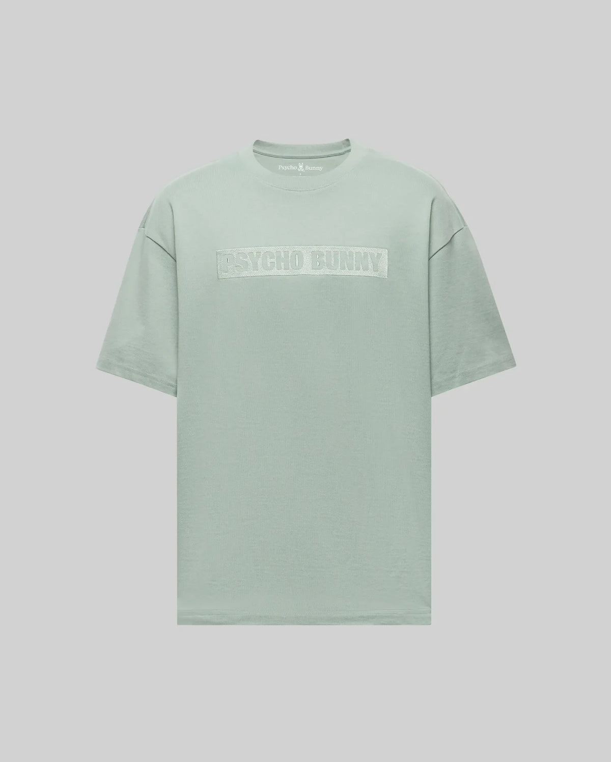 The Psycho Bunny MENS ZAYN OVERSIZED GRAPHIC TEE (MT0200004) is a pastel green heavyweight jersey short-sleeve t-shirt featuring bold white "PSYCHO BUNNY" lettering on the chest, shown against a light gray background.