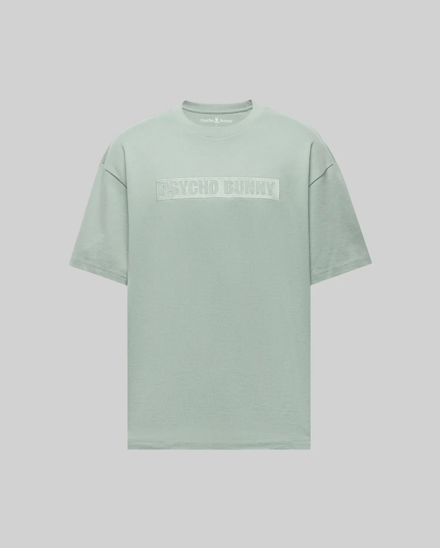 The Psycho Bunny MENS ZAYN OVERSIZED GRAPHIC TEE (MT0200004) is a pastel green heavyweight jersey short-sleeve t-shirt featuring bold white "PSYCHO BUNNY" lettering on the chest, shown against a light gray background.