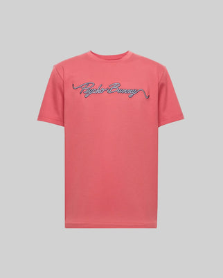 The Psycho Bunny MENS CYRUS WORDMARK GRAPHIC TEE (MT0200018) is a coral pink Pima cotton short-sleeve shirt with "Psycho Bunny" in blue and white cursive across the chest, shown on a plain light gray background.