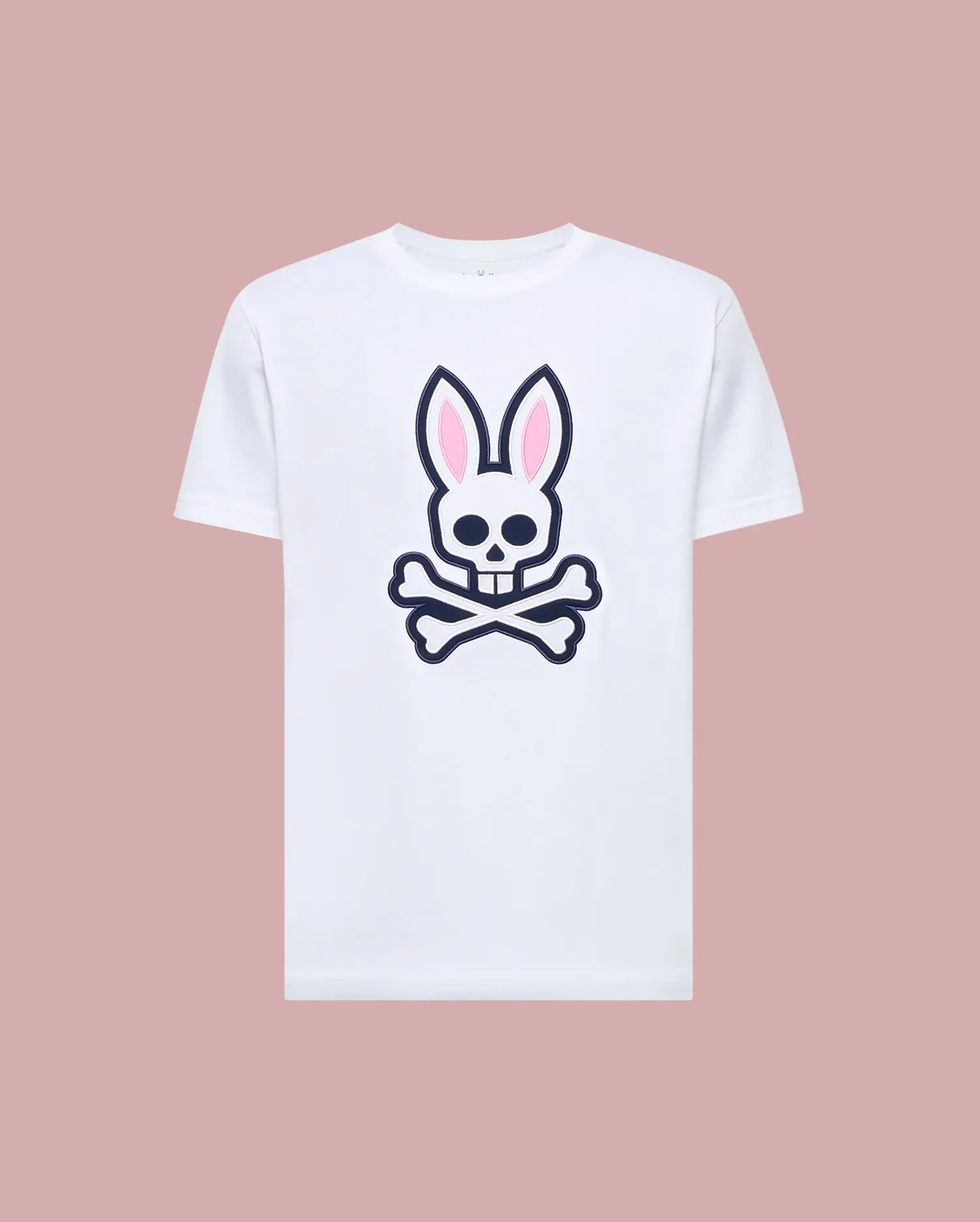 The Psycho Bunny MENS ARCHIVE BUNNY GRAPHIC TEE (MT0200031) is a white Pima cotton t-shirt featuring a large skull with bunny ears and crossbones graphic on the front, rib knit crewneck, shown against a muted pink background.