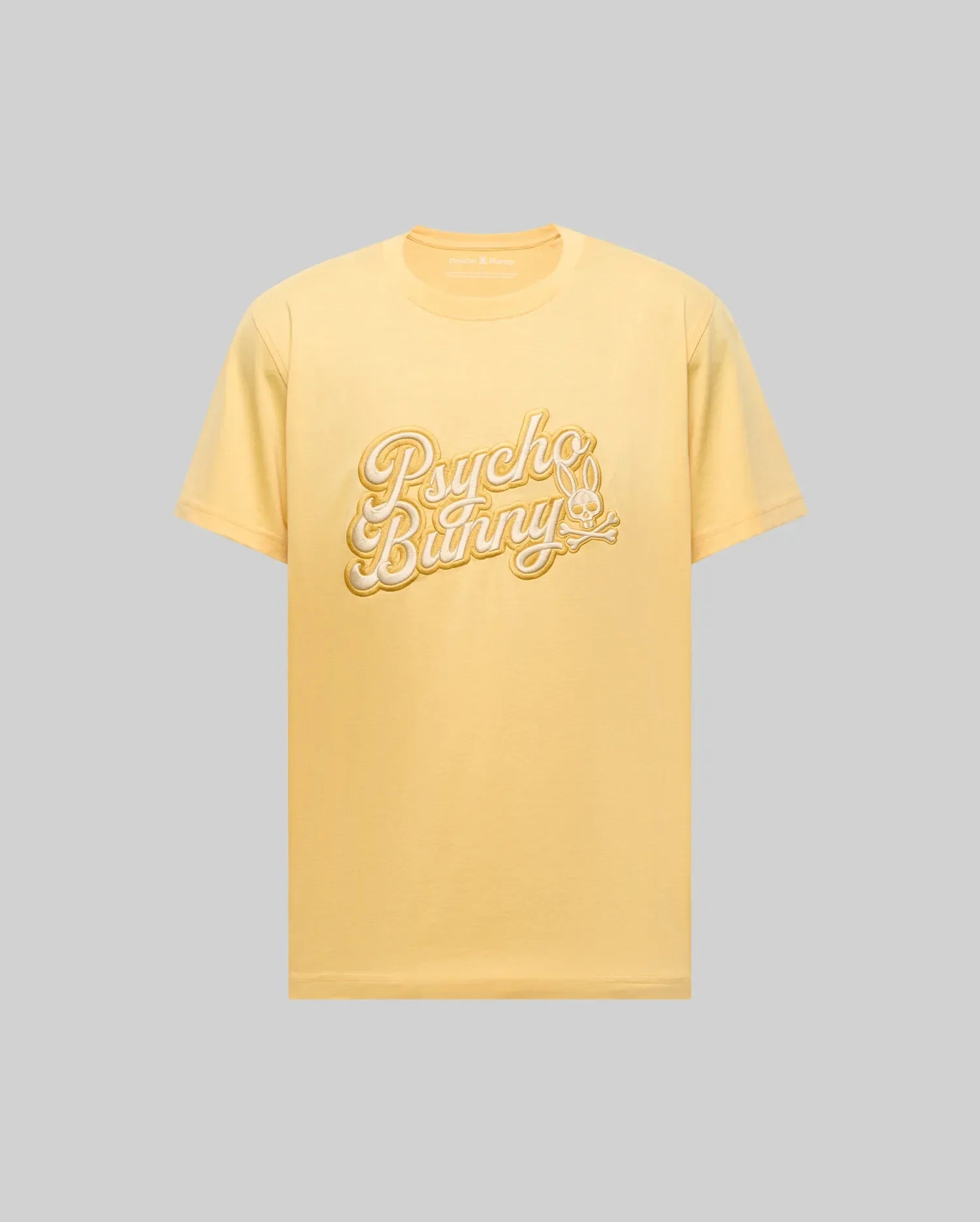 The Psycho Bunny MENS ELIAS GRAPHIC TEE (MT0200047) is a light yellow Pima cotton shirt featuring "Psycho Bunny" in bold white script and a retro bunny with crossbones graphic, shown on a plain gray background.