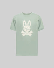 The Psycho Bunny MENS DEREK CENTER GRAPHIC TEE (MT0200048) is a light green Pima cotton short-sleeve shirt with a large white Bunny head and crossed bones graphic, plus "Psycho Bunny" cursive embroidery on the rabbit's face.