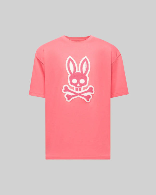 The Psycho Bunny MENS RYDER OVERSIZED FIT TEE (MT0200062) is a pink premium shirt with a large white bunny skull and crossbones graphic on the front, shown against a plain gray background.