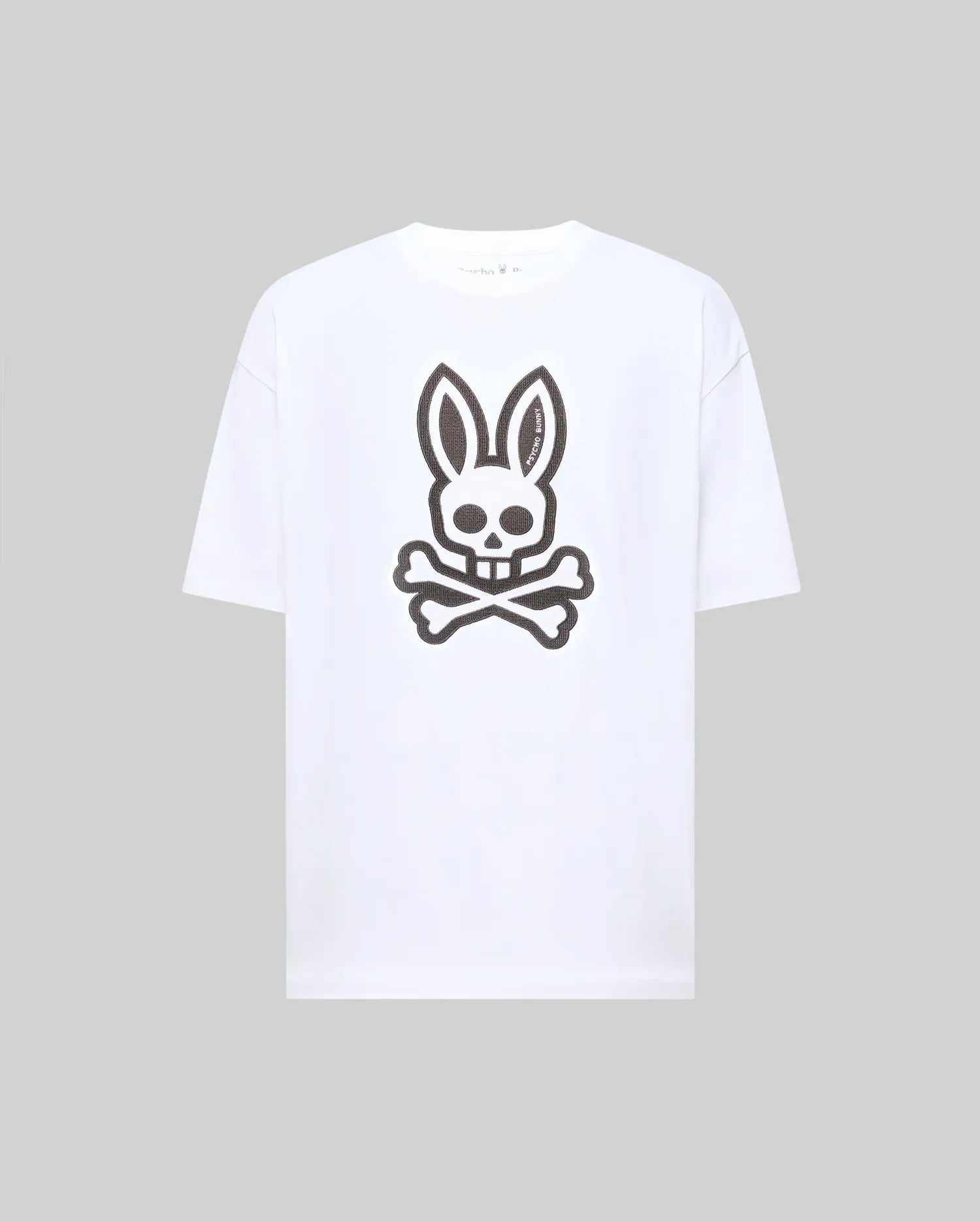 The Psycho Bunny MENS RYDER OVERSIZED FIT TEE (MT0200062) is a premium white Pima cotton T-shirt with an oversized fit, featuring a large black bunny skull and crossbones graphic on the front.