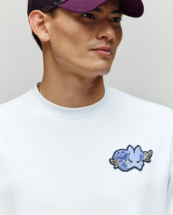 A person in a deep purple cap and the Psycho Bunny MENS AUGUSTE OVERSIZED TEE (MT0200104), with an embroidered Bunny logo on the chest, gazes sideways against a neutral backdrop for an effortlessly laidback look.