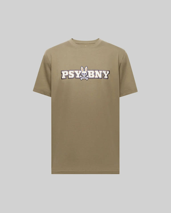 The Psycho Bunny MENS WADE GRAPHIC TEE - MT0200105 is a khaki 100% cotton shirt showcasing "PSYBNY" text and a cartoon bunny skull and crossbones graphic at the center, set against a plain light gray background.