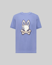 The Psycho Bunny MENS WADE GRAPHIC TEE (MT0200106) is a light purple 100% cotton shirt featuring a large white cartoon bunny head with crossbones on the front.